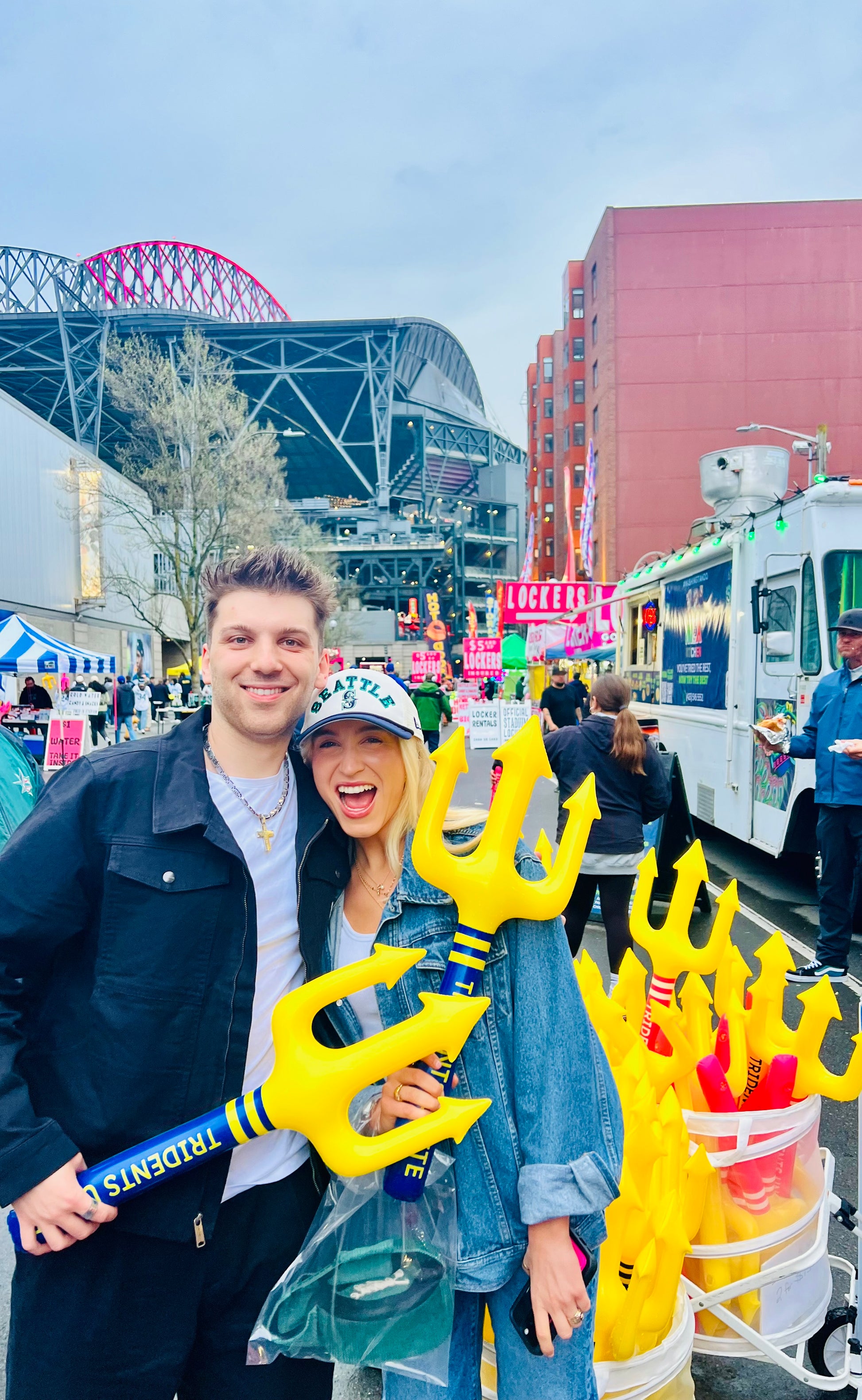 Two people holding yellow tridents in front of T-mobile stadium and cityscape. Seattle. Trident. Tridents Unite